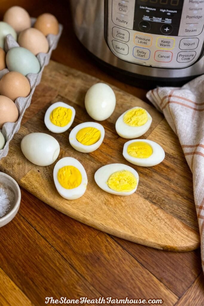 Peeled and halved hard boiled eggs with bright yellow yolks arranged on a wooden cutting board beside an Instant Pot.