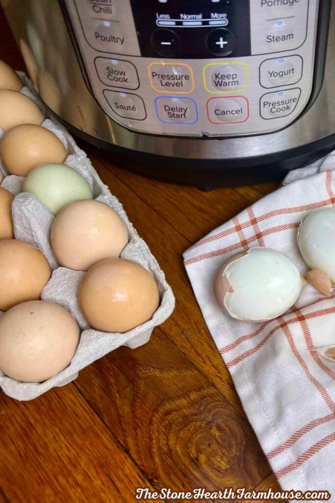 Fresh brown and blue-green eggs in an egg carton beside an Instant Pot, with a peeled egg resting on a plaid kitchen towel.