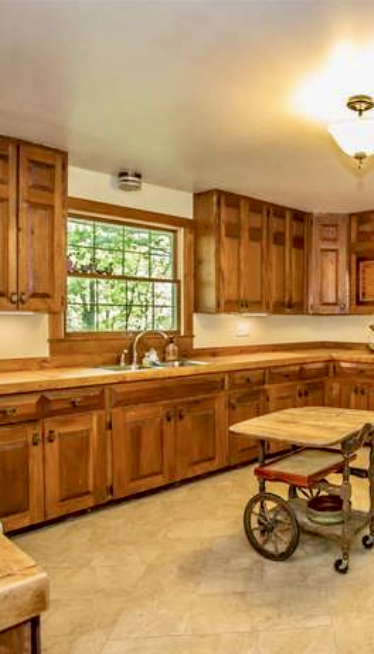 Warm-toned kitchen featuring custom oak butcher block countertops and handcrafted wooden cabinets, with a rustic rolling island in the center.