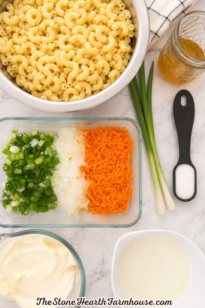 Ingredients for Hawaiian macaroni salad arranged on a light marble countertop with cooked pasta, carrots, green onions, mayonnaise, and dressing