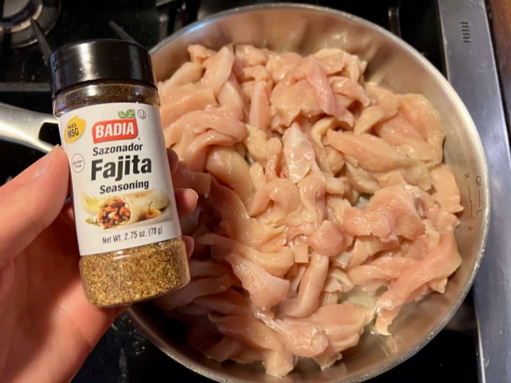chicken strips being cooked in a shillet and a hand holding the fajita seasoning container.