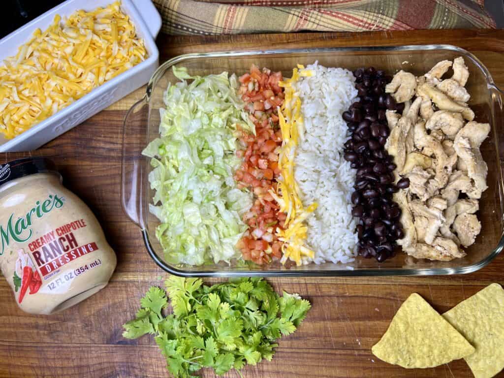 featuring salad ingredients in a pan nicely separated to display. lettuce, salsa, cheese, rice, black beans, chicken. Also shows the dressing I used and cheese.