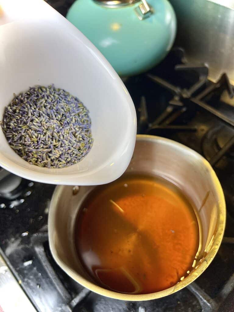 A person is pouring lavender into a pot with honey.