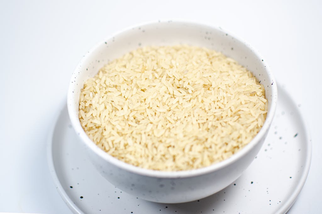 A close-up shot of uncooked rice grains in a speckled white bowl on a matching plate.