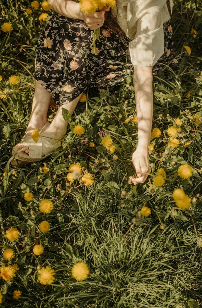 A woman in floral skirt sits picking yellow flowers in a sunny meadow, capturing a serene moment.