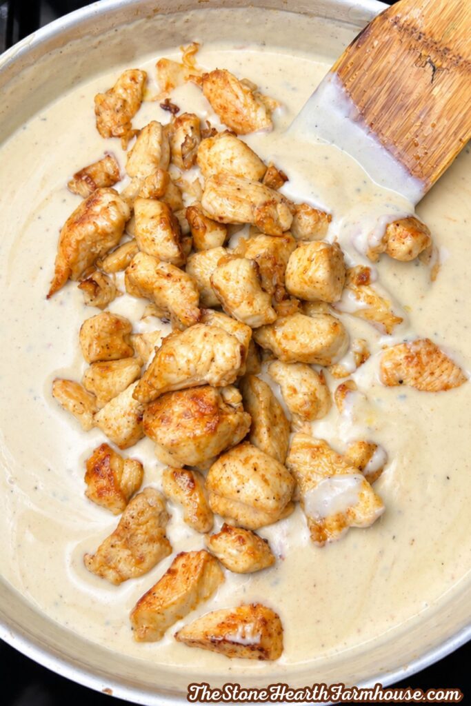 Seared chicken pieces added to a skillet of creamy seasoned sauce