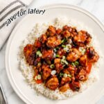 Sweet Chili Rabbit served over white rice with colorful peppers and green onions on a white plate, photographed on a marble countertop.