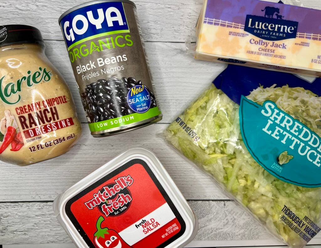 Ingredients for Southwest chicken salad including creamy chipotle ranch dressing, black beans, Colby Jack cheese, lettuce, and fresh salsa