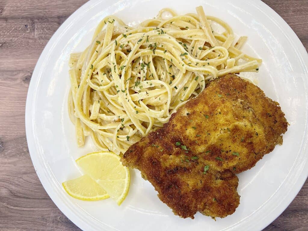A plate of lemon chicken pasta with a slice of lemon.