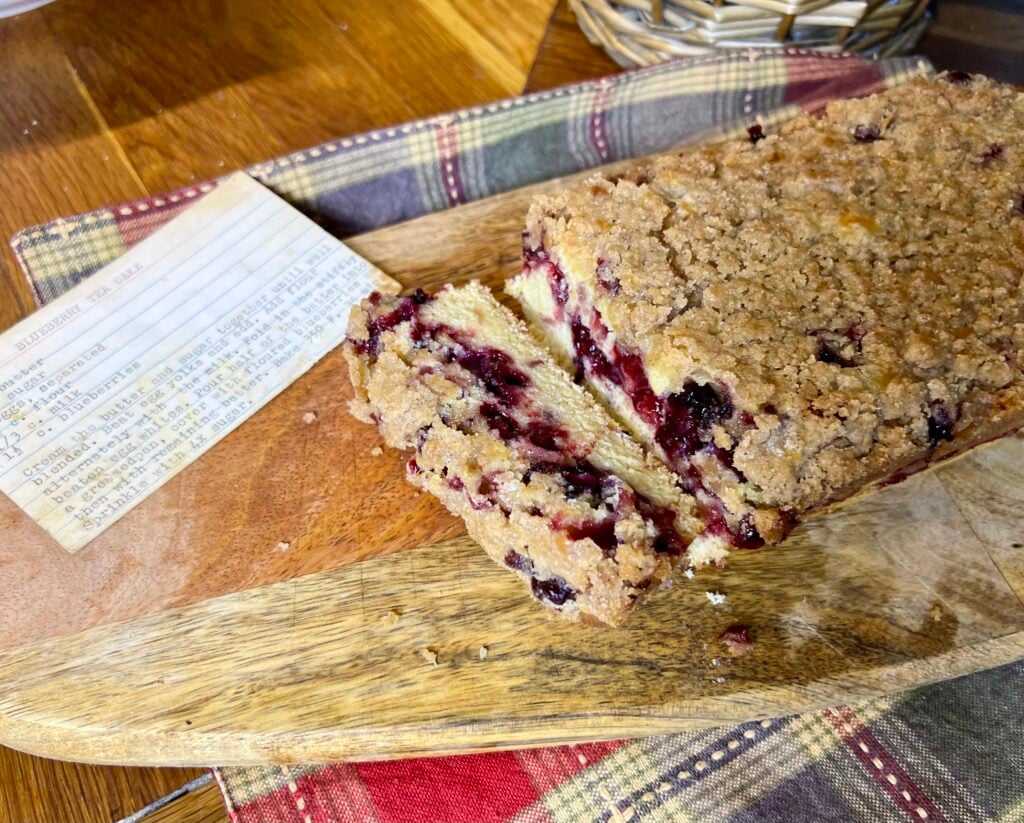 sliced blueberry tea cake on a wooden cutting board.