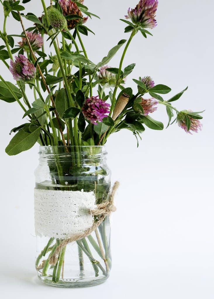 A charming bouquet of red clover flowers arranged in a decorated glass jar with natural twine.