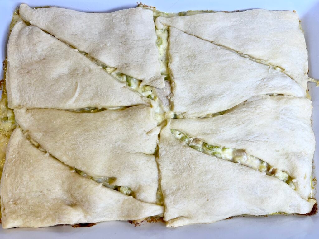 The crescent rolls are rolled out on the top of the filling in the casserole dish and ready to be baked.