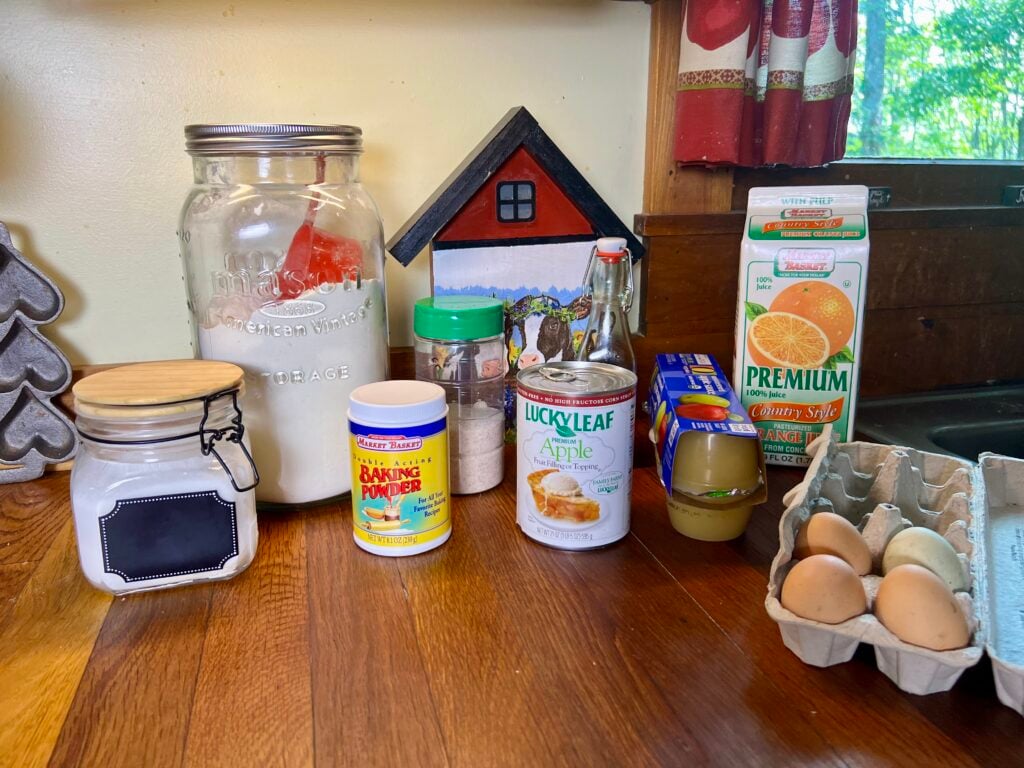 All of the ingrediense needed to make this fall apple Bundt cake recipe, on a counter. sugar, flour, baking powder, apple pie filling, apple sauce, orange juice, salt, and eggs.