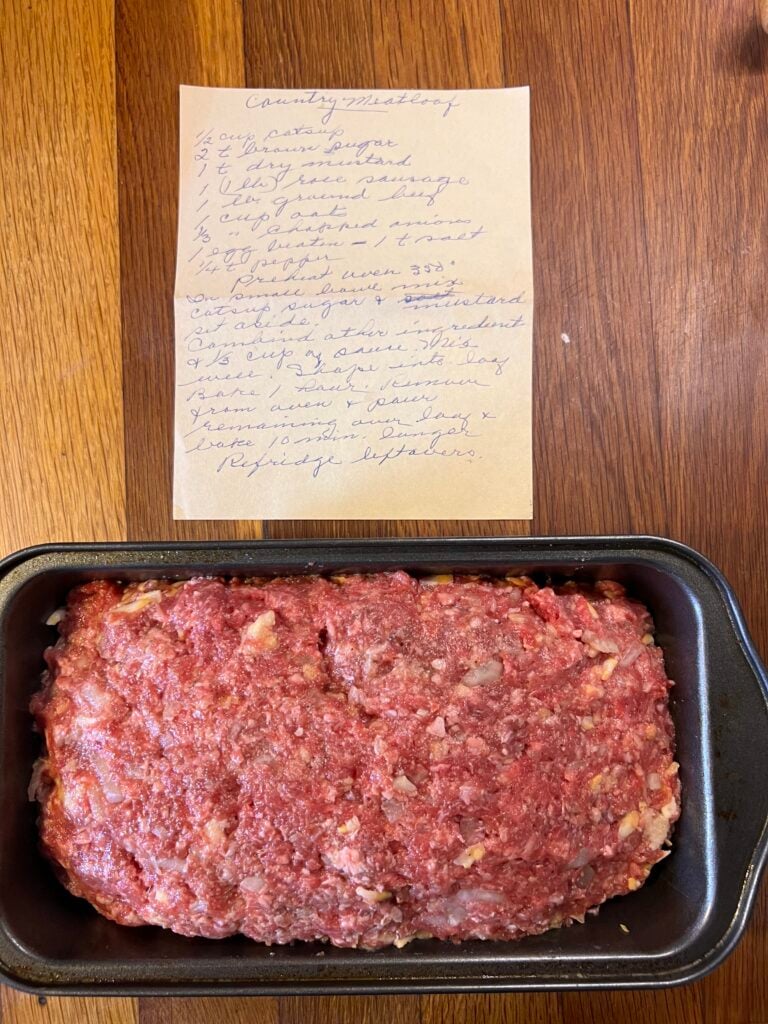 meatloaf ready to go into the oven sitting next to the old fashioned recipe card. 