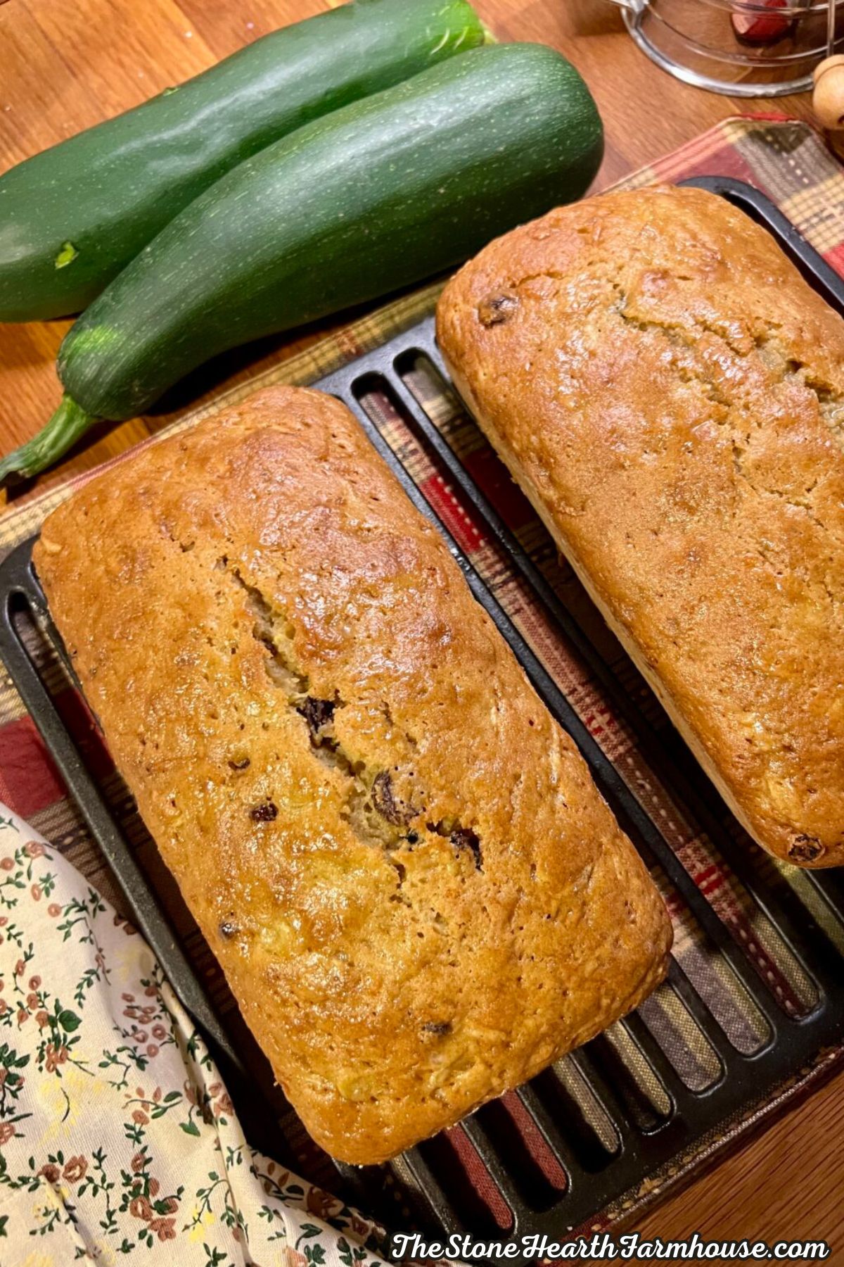 Two golden-brown loaves of homemade zucchini bread with raisins on a baking tray, showing the moist texture and crisp baked crust.