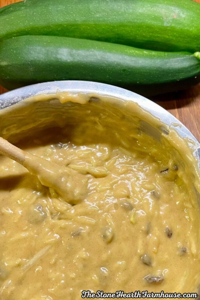 Thick homemade zucchini bread batter with shredded zucchini and raisins being stirred in a mixing bowl.