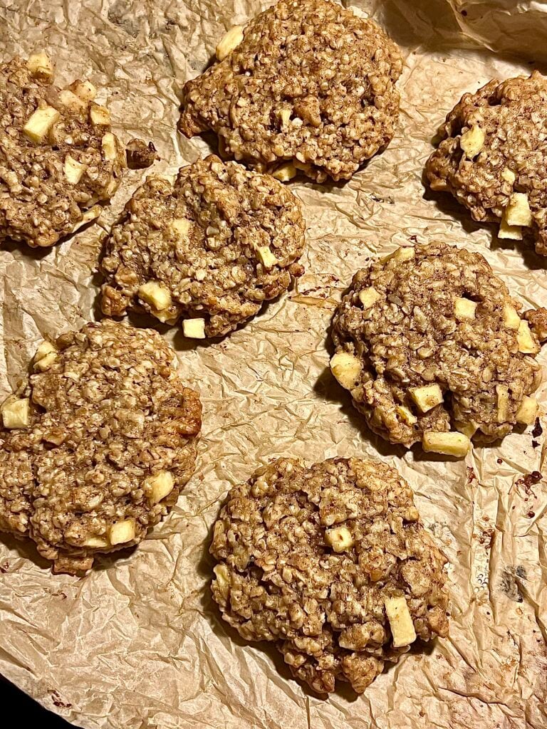 Yummy! These are a close up of the freshly baked cinnamon apple and oatmeal cookies out of the oven. The cookies are on the sheet pan with brown parchment paper. 