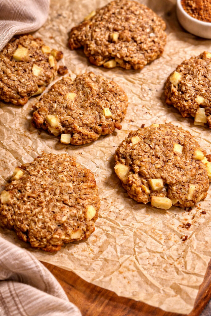 Yummy! These are a close up of the freshly baked cinnamon apple and oatmeal cookies out of the oven. The cookies are on the sheet pan with brown parchment paper. 