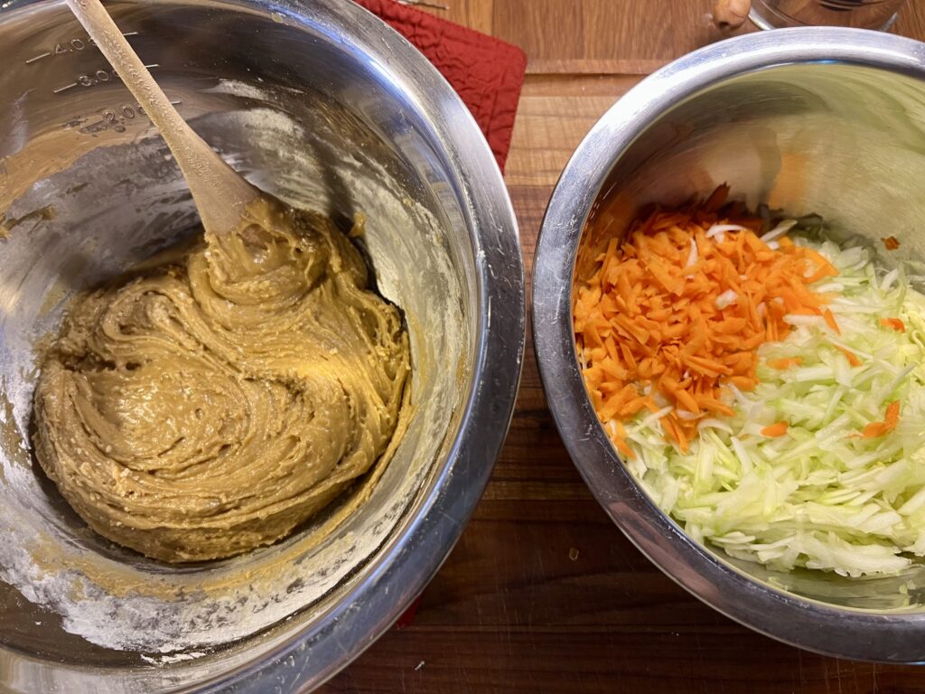 Two bowls. One is filled with the batter for the carrot and zucchini bread recipe. The other bowl is filled with shredded carrots and zucchini that is ready to be mixed into the batter. 