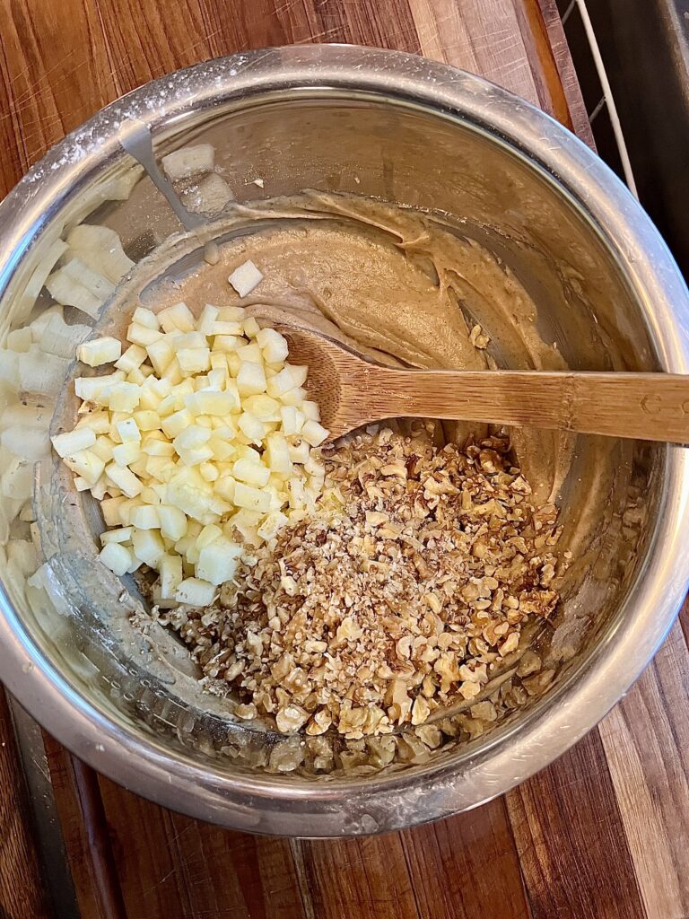 Apple and oatmeal cookie ingredients being mixed together in a bowl, with chopped apples and diced walnuts. 
