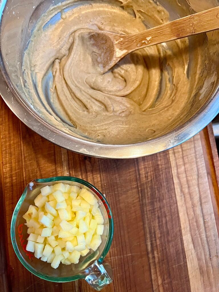 This is a bowl of the fall cookie batter and next to it is one cup of diced apples, ready to be mixed in the batter. 