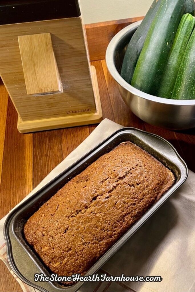 Homemade zucchini bread baked with fresh milled flour, served beside a grain mill and fresh garden zucchini.