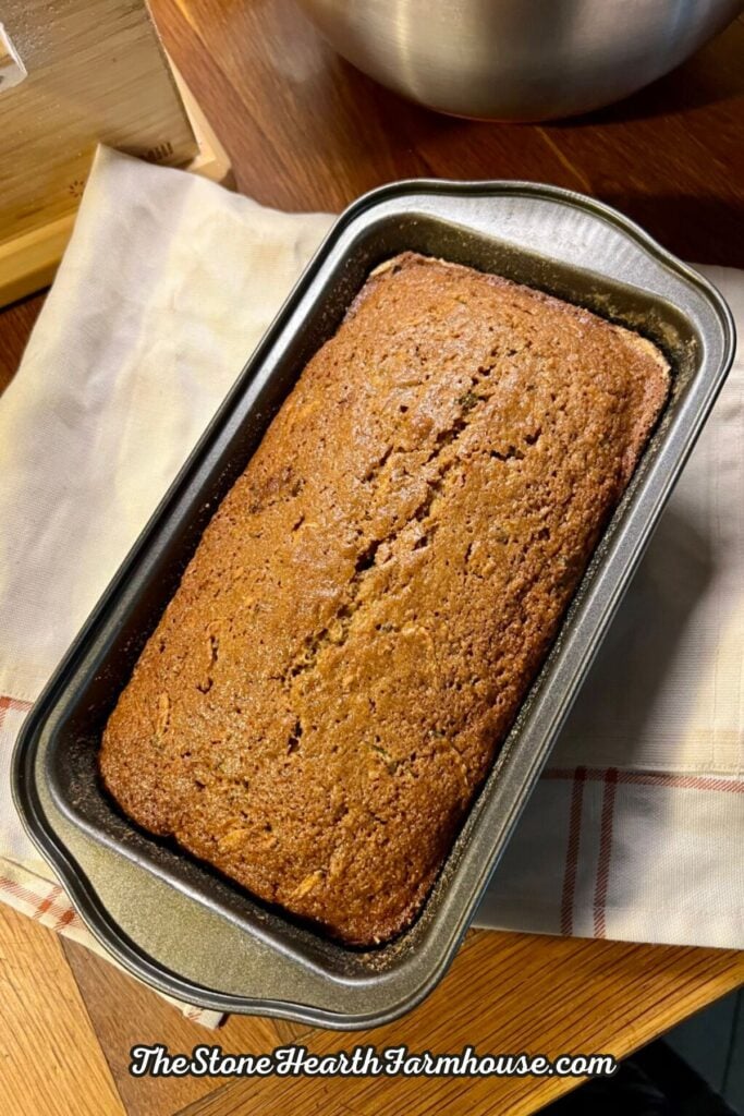 Freshly baked zucchini loaf cooling in a bread pan with a golden brown crust and homemade farmhouse style.