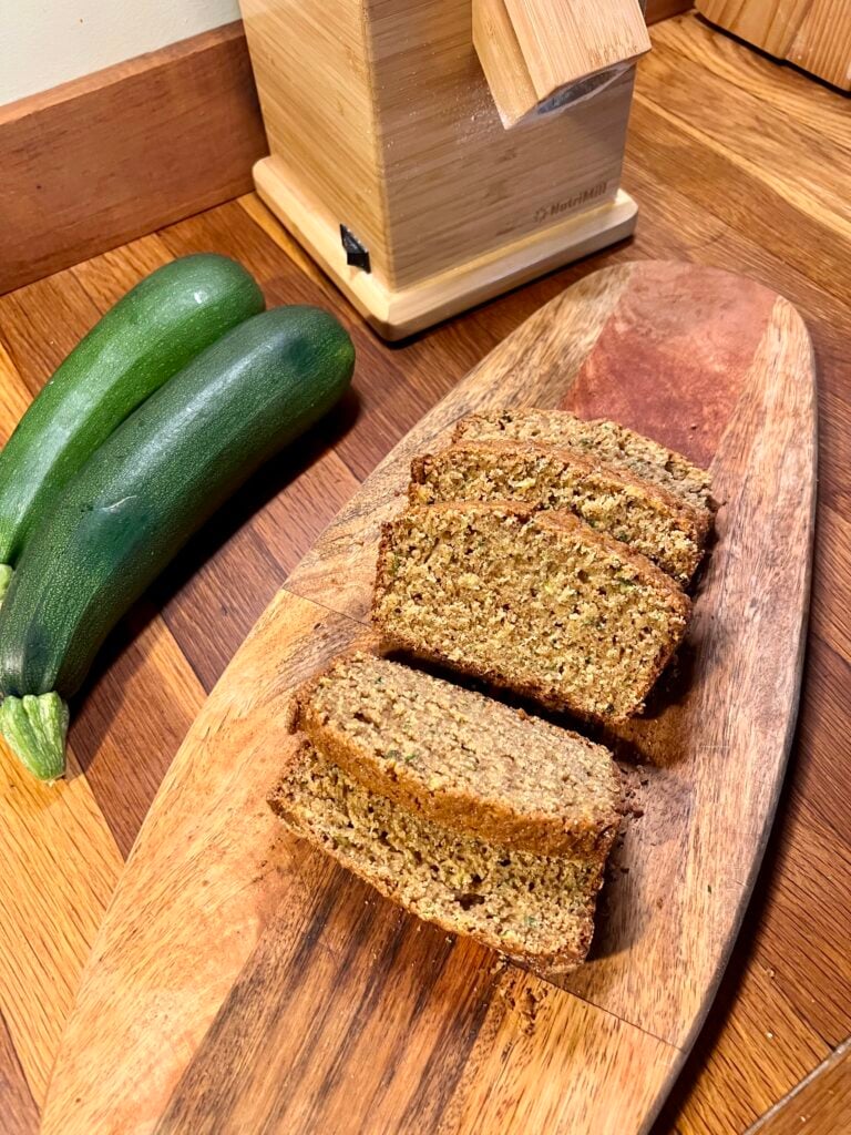 sliced zucchini quick bread on a cutting board next to some zucchini. 