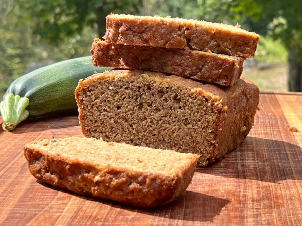 the best fresh milled zucchini bread on a wooden cutting board , sliced and next to a zucchini.
