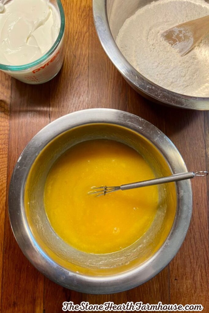 Melted butter in a mixing bowl with a whisk alongside flour and sour cream for baking.