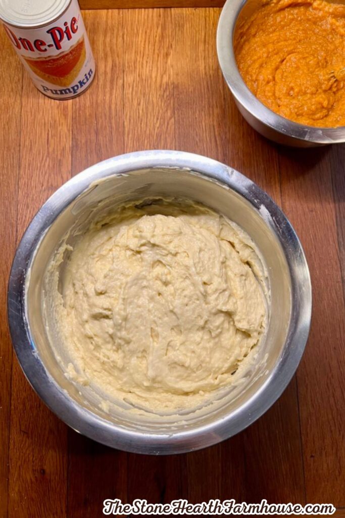 Thick pumpkin cake batter mixed in a stainless steel bowl with pumpkin puree visible in the background.