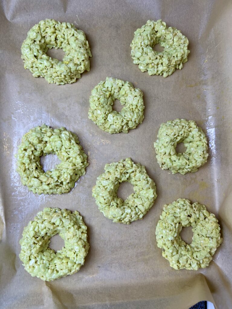 Small Rice Krispie wreath treats shaped into rings and cooling on a parchment-lined baking sheet.
