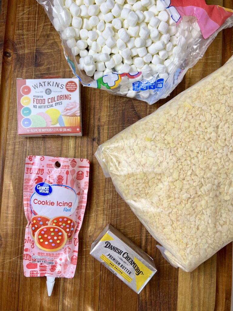 Ingredients for making Rice Krispie Christmas wreaths, including marshmallows, cereal, butter, food coloring, and red cookie icing.