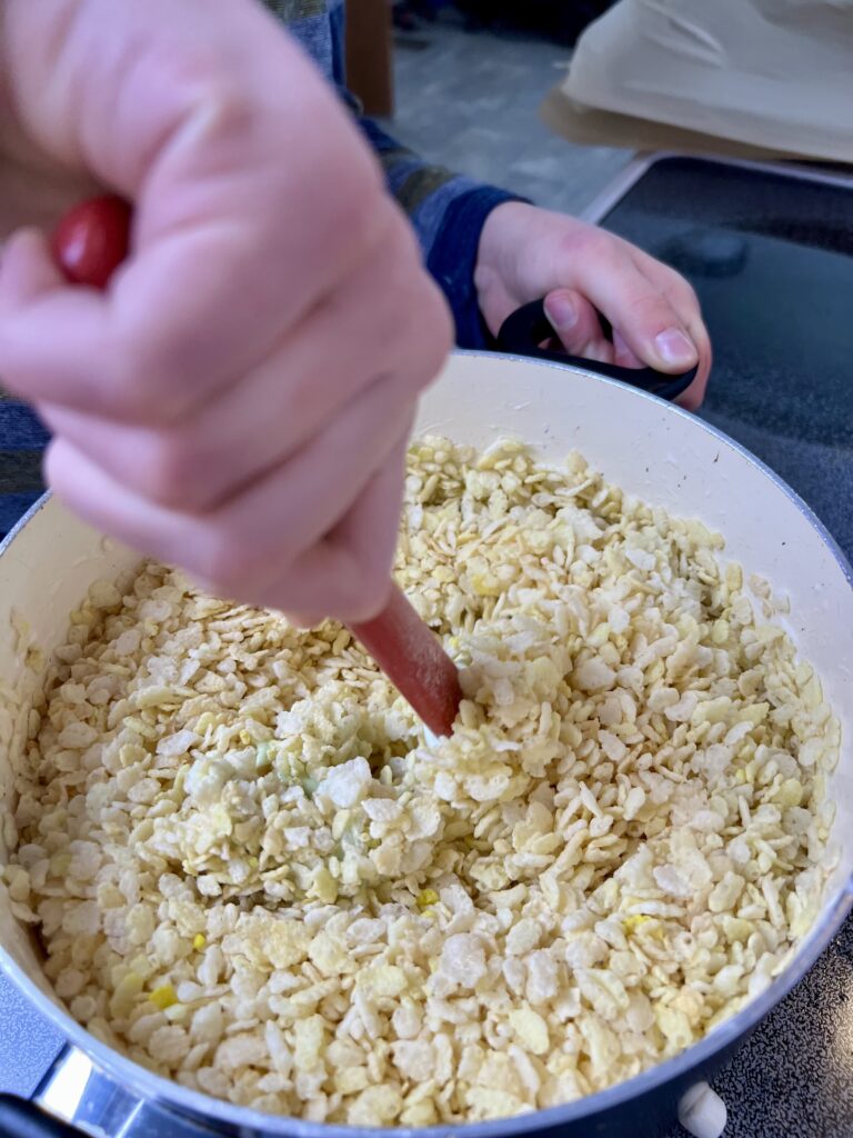 Child stirring Rice Krispies into melted marshmallows in a pot while making Christmas wreath treats.