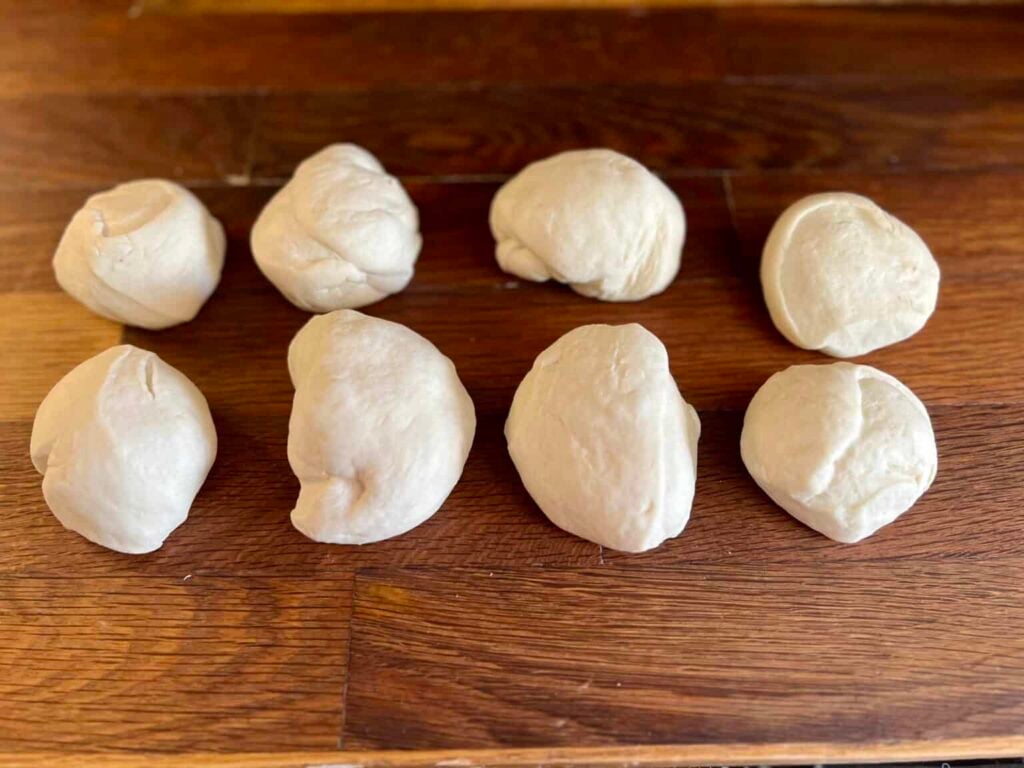 Portioned sourdough soft pretzel dough balls resting on a wooden surface, ready to be rolled and shaped into pretzels.