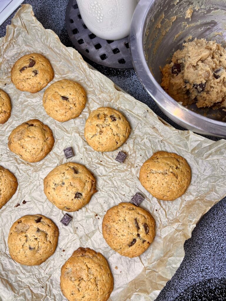Brown butter sourdough chocolate chip cookies cooling on parchment paper with cookie dough and chocolate chunks