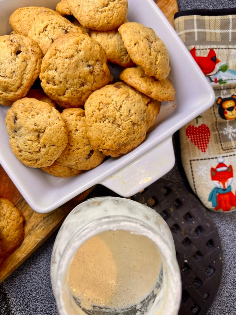 Freshly baked brown butter sourdough chocolate chip cookies stacked in a baking dish with sourdough starter nearby