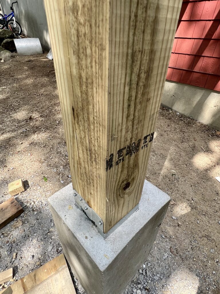 Close-up of pressure treated deck post secured to concrete footing with metal post base