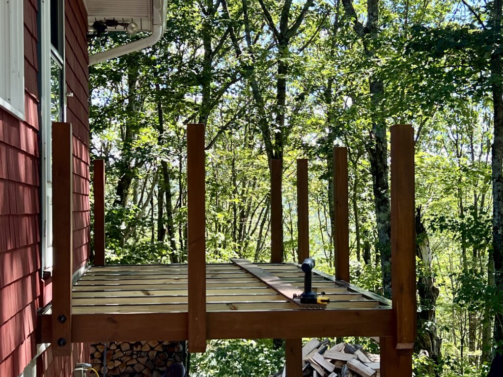 DIY deck framing attached to house with vertical posts installed and joists in place