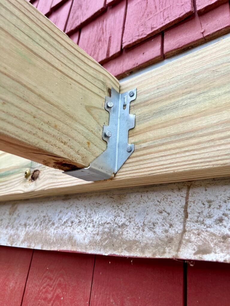 Close-up of galvanized joist hanger securing deck framing to beam during DIY deck construction
