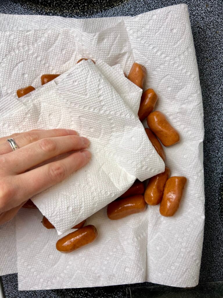 hand drying the mini sausages, on a paper towel lined plate to absorb juices. 