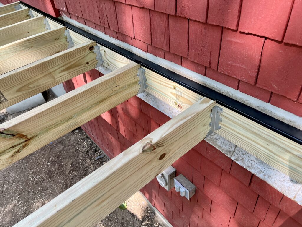 Deck ledger board attached to house with joist hangers during DIY deck framing