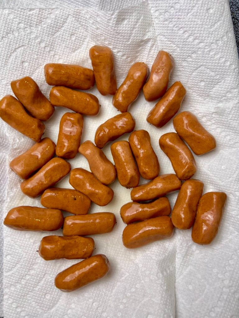 this is showing the mini sausages on a paper plate with a paper towel on it to help absorb some of the juices from the mini hot dogs.