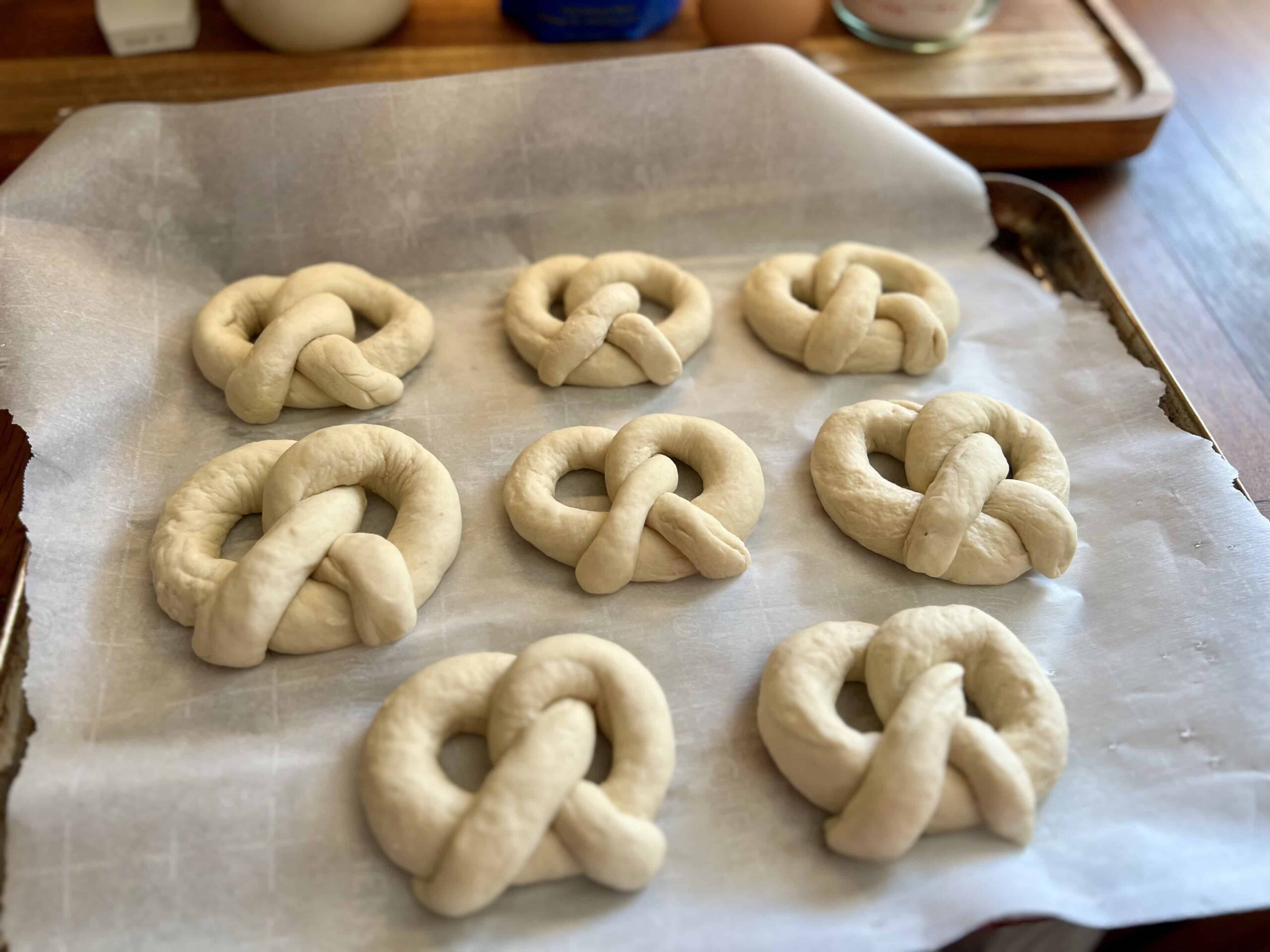Unbaked sourdough soft pretzels shaped and arranged on a parchment-lined baking sheet, ready for boiling and baking.