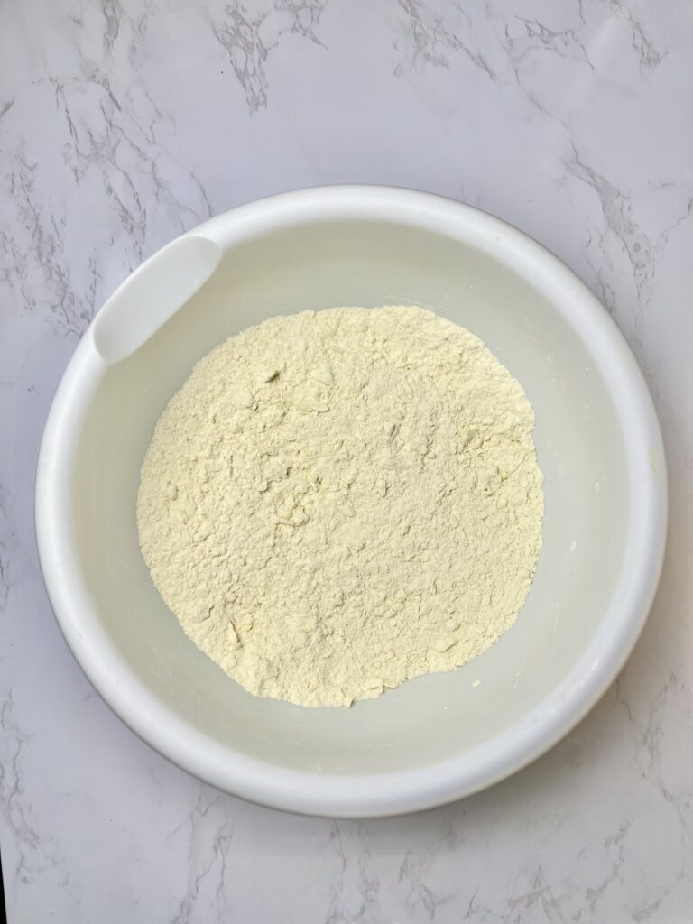 Mixed dry ingredients for pigs in a blanket dough in a white bowl, showing flour blended with salt and butter before adding wet ingredients.