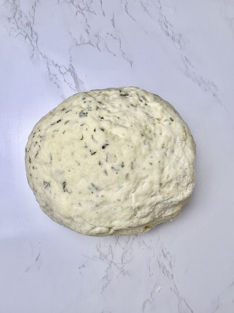 Herbed dough ball resting on a floured surface, prepared for homemade pigs in a blanket before rolling and cutting.