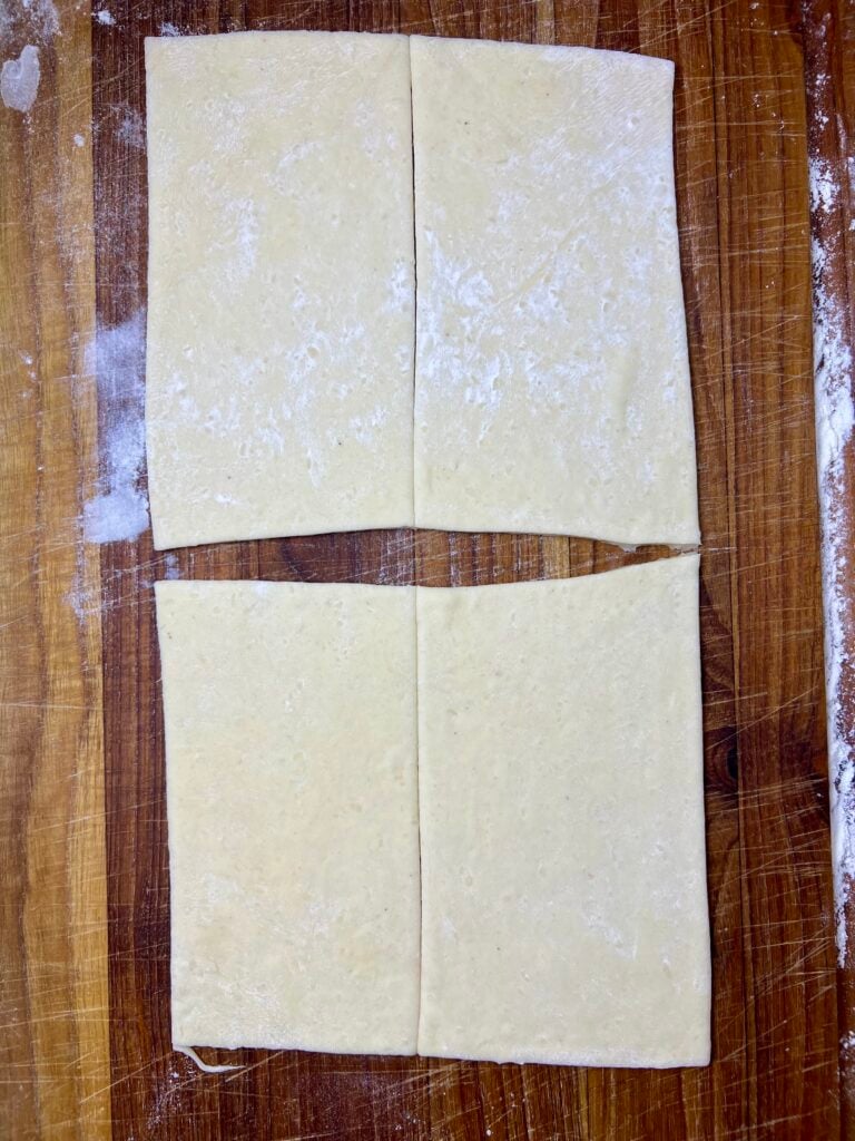 dough rolled out and cut into fourth on a wooden cutting board for pigs in a blanket. 