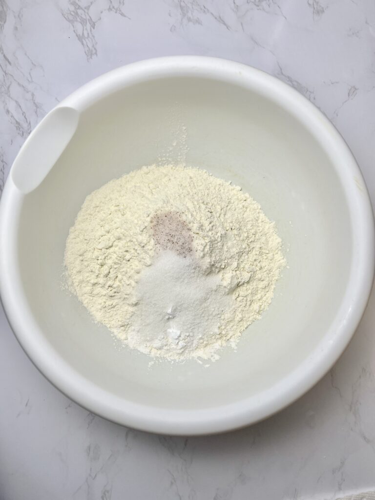 Dry ingredients for pigs in a blanket dough in a white mixing bowl, including flour, salt, sugar, and seasoning, ready to be mixed for homemade pigs in a blanket.