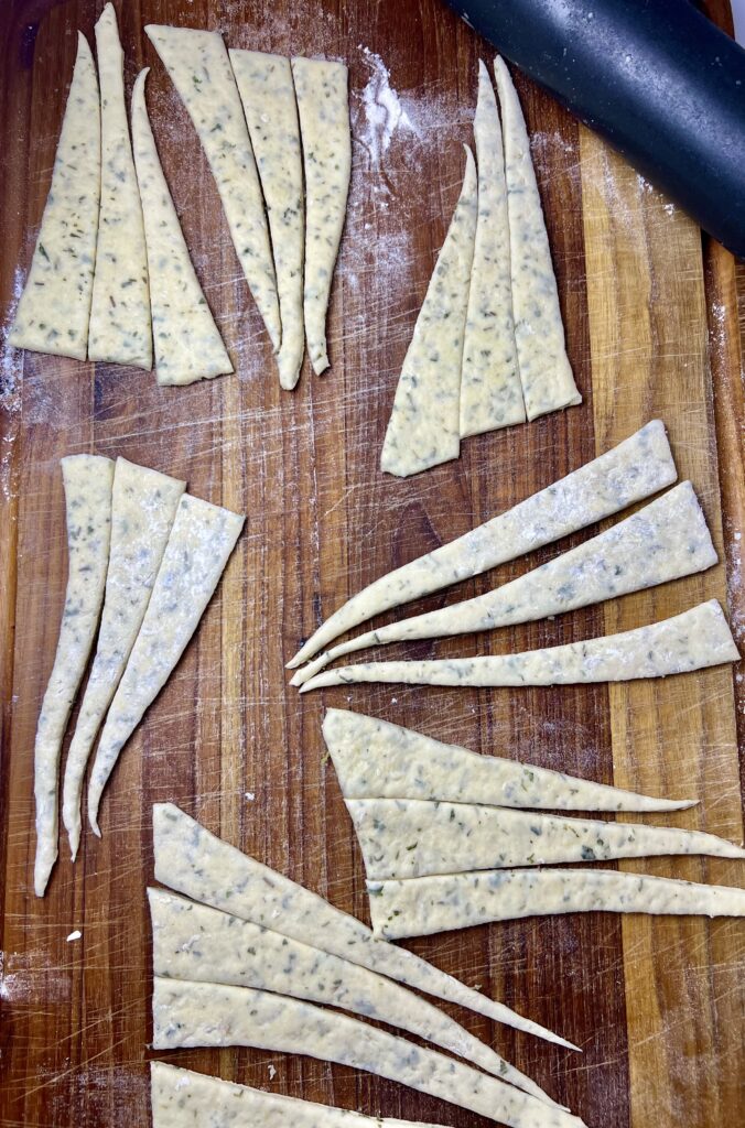 Herbed dough cut into thin triangles and strips on a floured wooden cutting board, prepared for wrapping around mini sausages to make homemade pigs in a blanket.