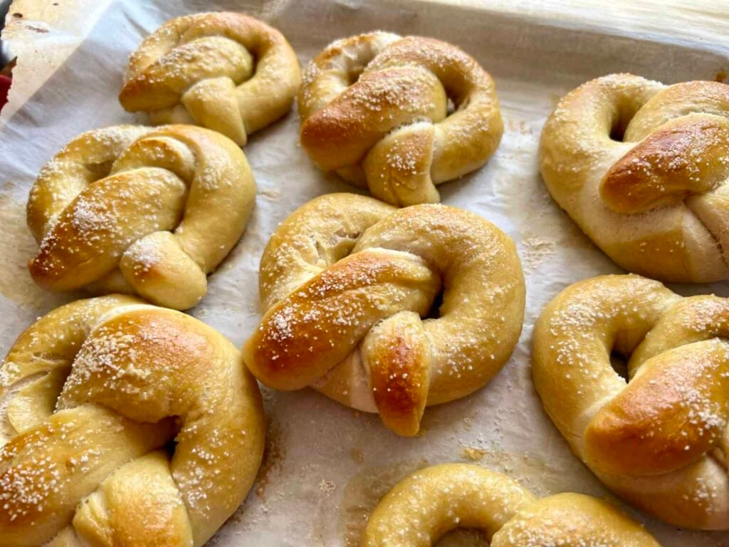 Golden brown sourdough soft pretzels fresh out of the oven, sprinkled with coarse salt on a parchment-lined baking sheet.